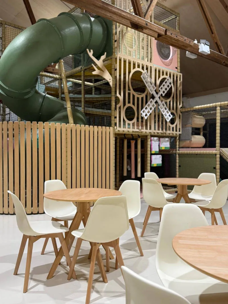 Inside soft play center showing cafe tables and chairs with slide in the background